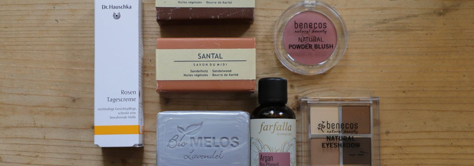 Holzregal mit Naturkosmetik: Tiegel, Flaschen und Kartonverpackungen in Reihen, dazu Seifen und Bürsten